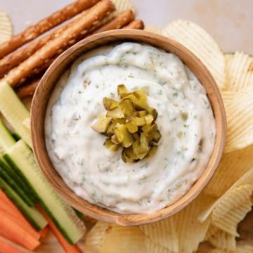 overhead of a bowl of dill pickle dip with chopped pickles on top, sitting on a tray with vegetables and chips